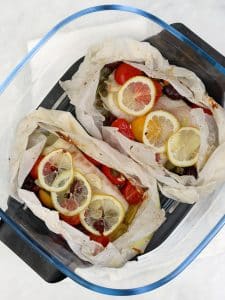 Two parchment parcels of cooked cod inside an air fryer basket