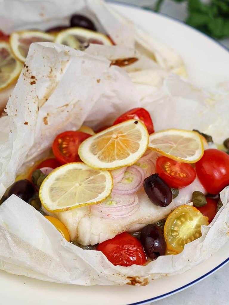 Two open parchment parcels of air-fried cod with cherry tomatoes, lemon, and kalamata olives