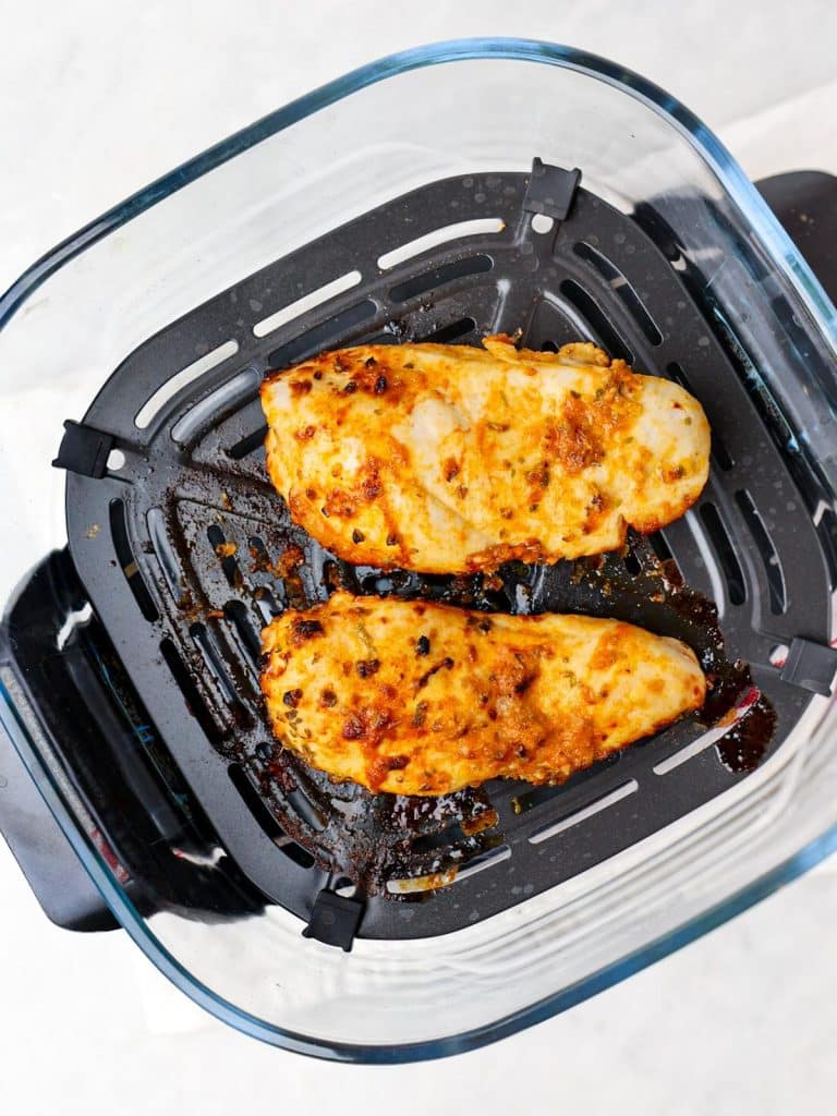 Two golden greek marinated chicken breasts in an air fryer basket