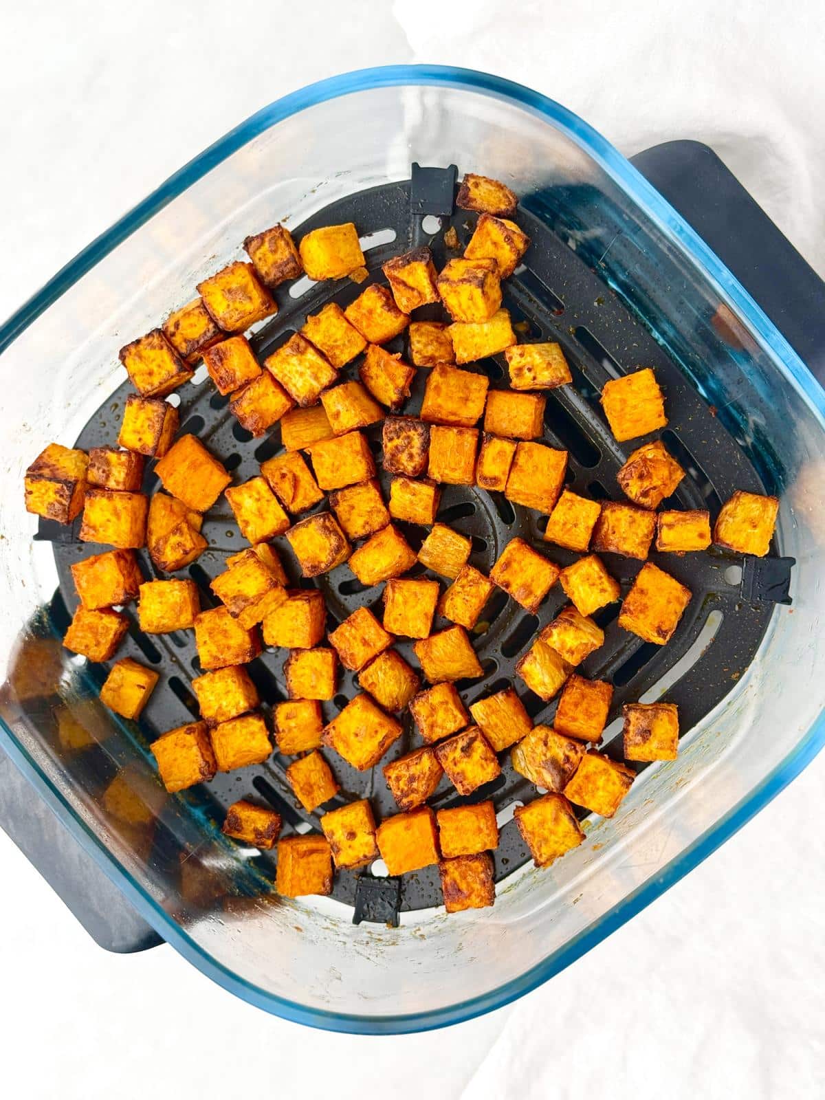 Seasoned roasted sweet potato cubes in an air fryer basket