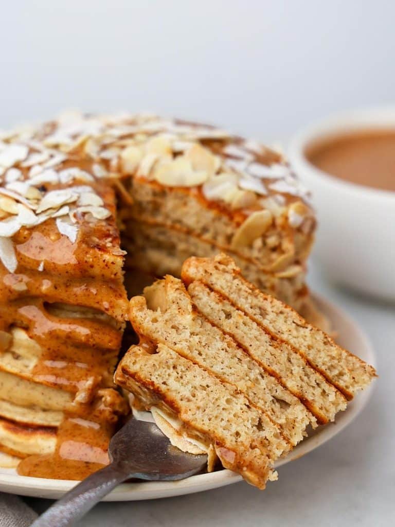 Fork lifting a slice of almond croissant pancakes showing fluffy interior layers with almond cream drizzle