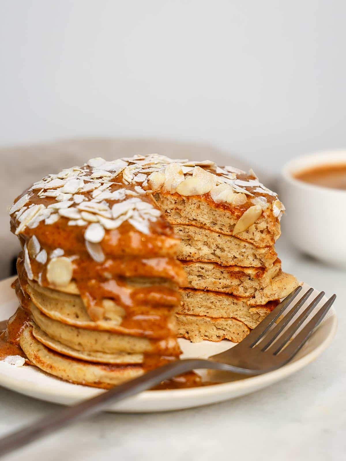 Tall stack of almond croissant protein pancakes with almond cream drizzle running down the sides and toasted sliced almonds on top