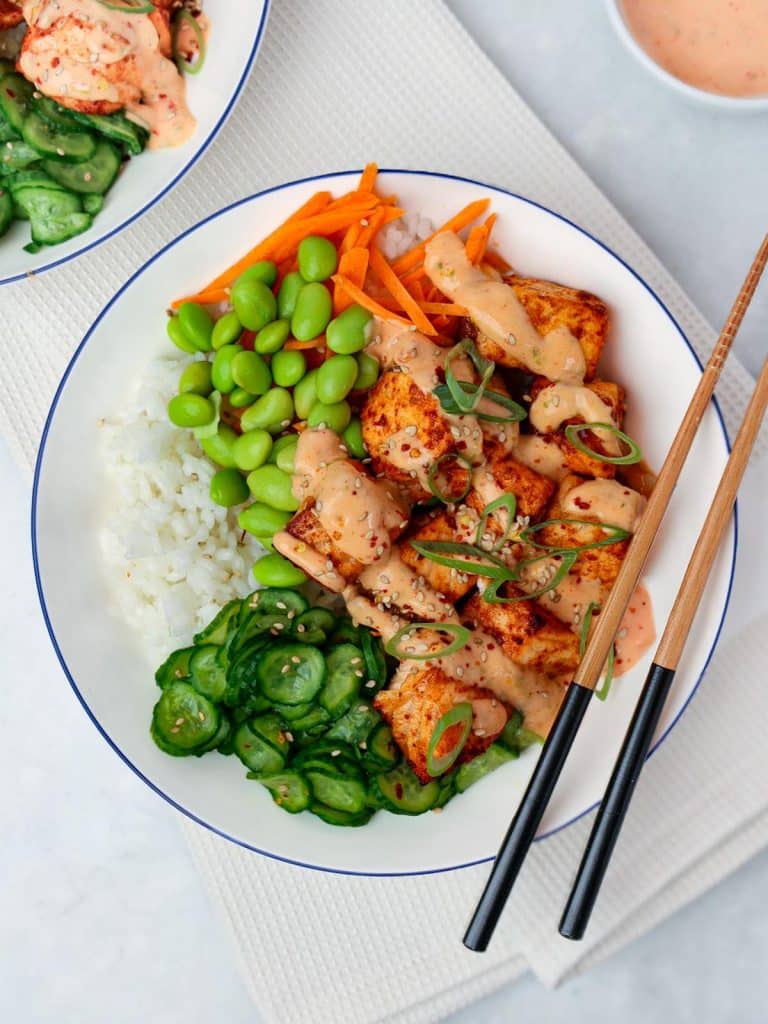 Overhead bang bang salmon bowl with rice, edamame, carrots and cucumbers