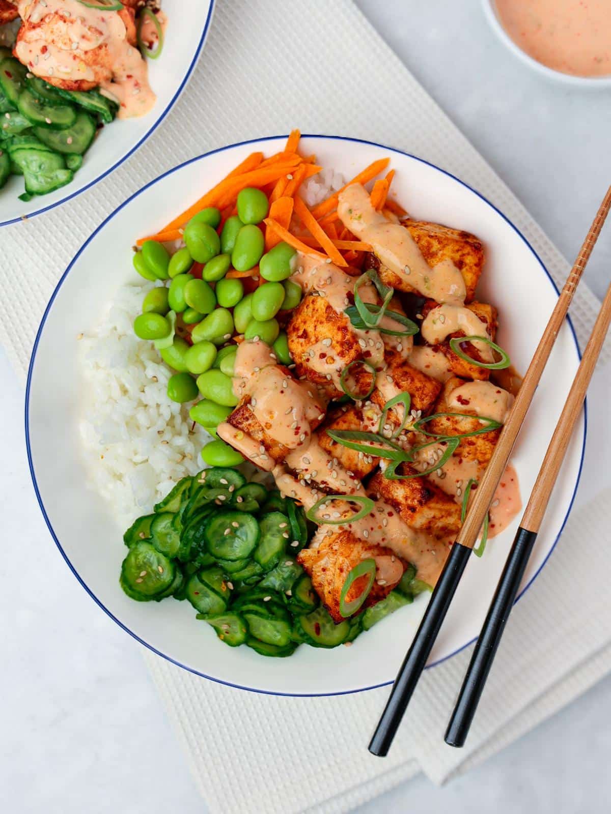 Overhead bang bang salmon bowl with rice, edamame, carrots and cucumbers