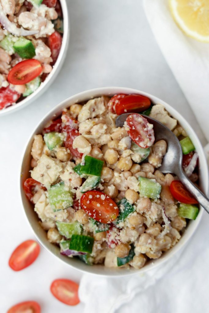 Two bowls of caesar bean salad with a lemon half and spoon