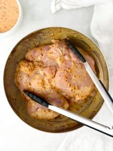 Chicken thighs marinating in hot honey mustard sauce with tongs
