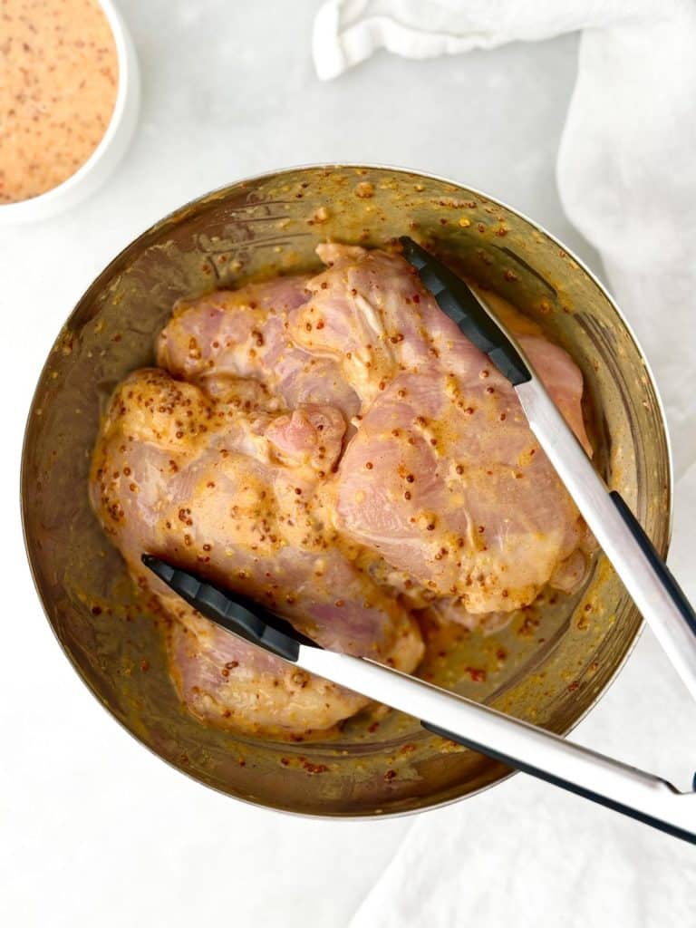 Chicken thighs marinating in hot honey mustard sauce with tongs