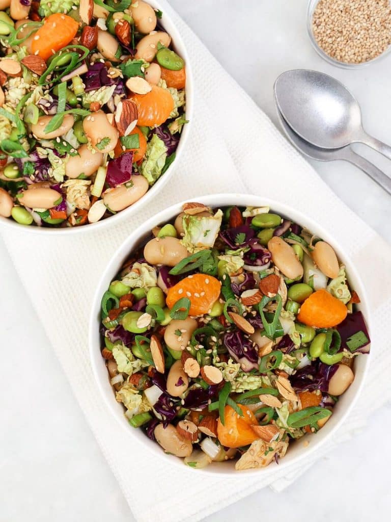 Two white bowls of chinese chicken dense bean salad with butter beans, edamame, mandarin, and almonds
