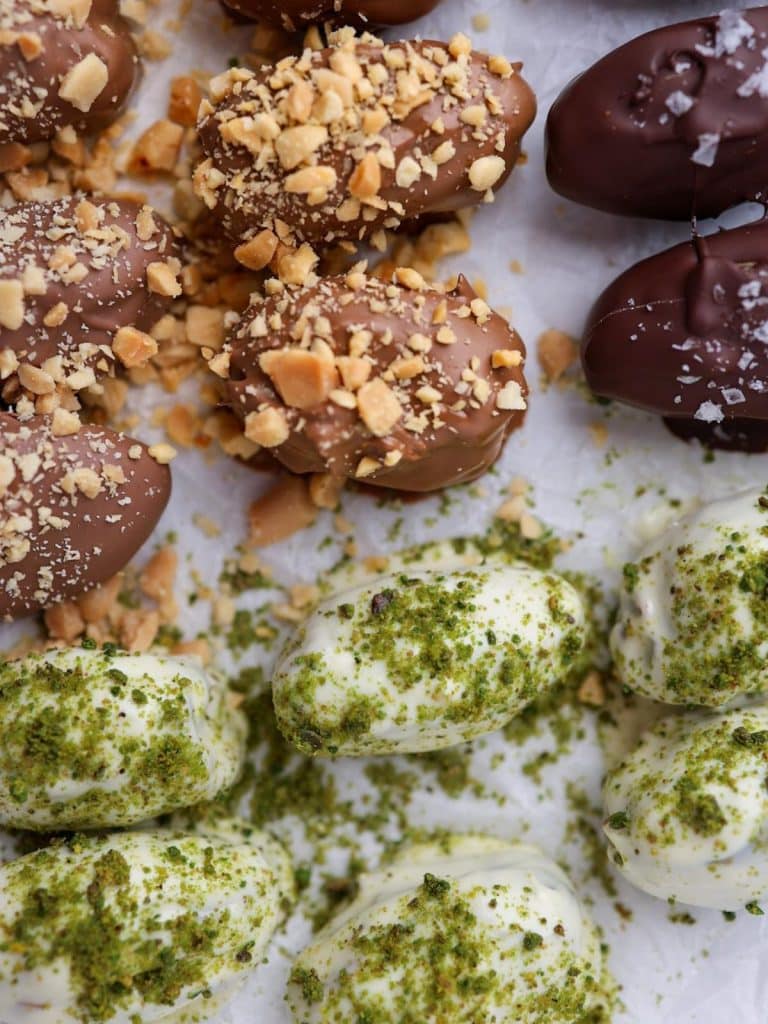 Milk chocolate peanut butter and white chocolate pistachio stuffed dates on parchment paper