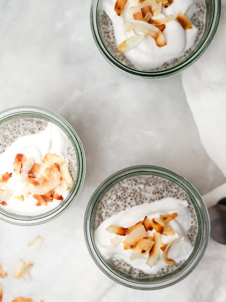 Three jars of coconut chia pudding topped with coconut yogurt and toasted coconut flakes
