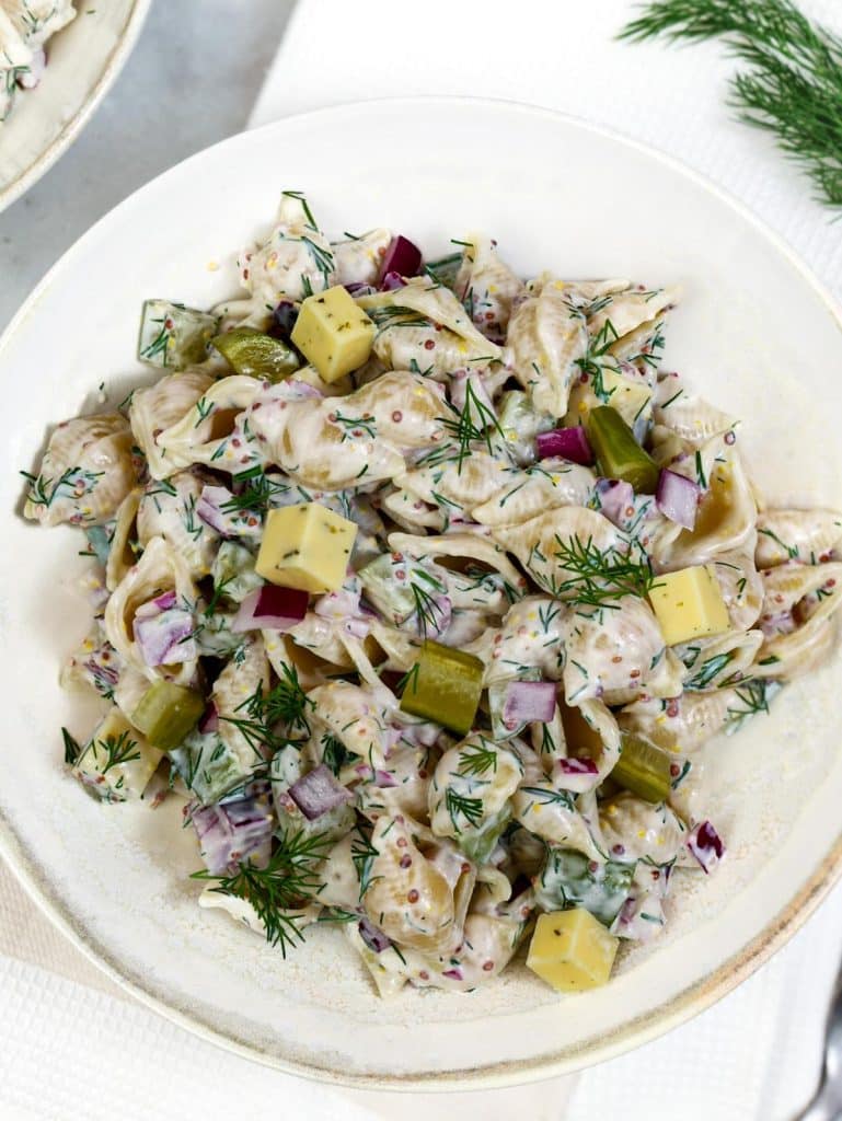 Creamy dill pickle pasta salad in a white bowl loaded with cheese cubes and fresh dill