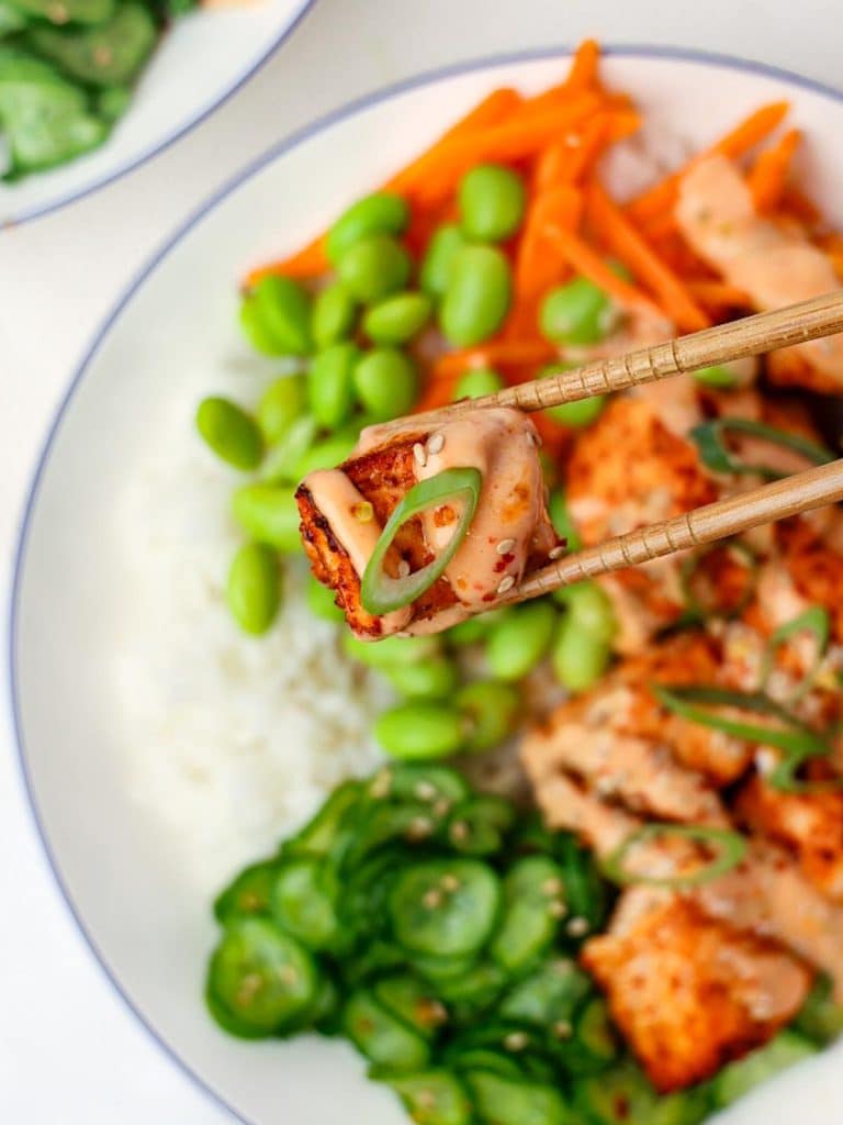 Chopsticks lifting a crispy salmon cube drizzled in bang bang sauce