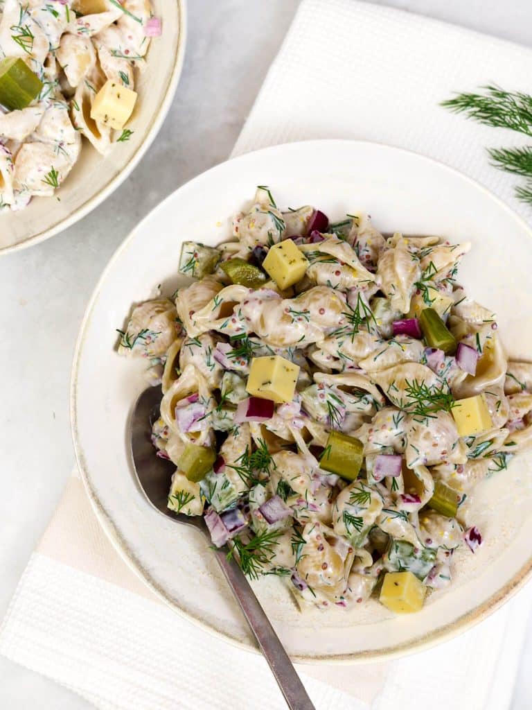 Dill pickle pasta salad with greek yogurt dressing in a white bowl with a spoon and fresh dill