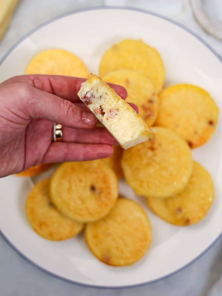 Hand holding a halved easy quiche lorraine egg bite over a plate of more bites
