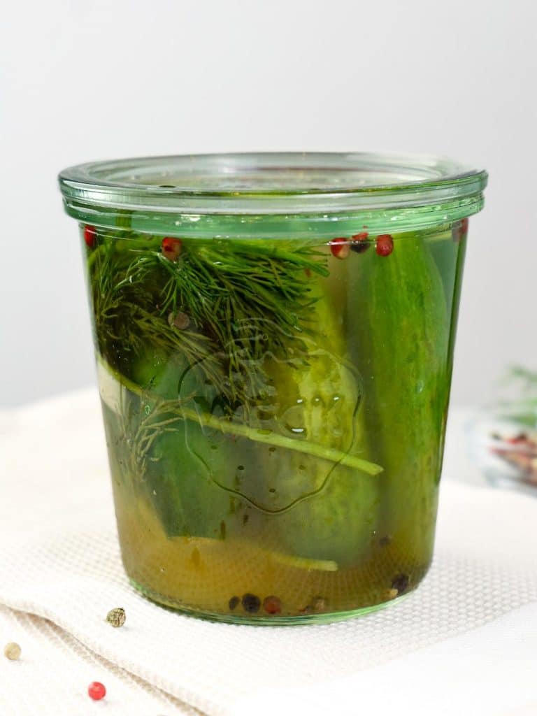 Weck jar of fermented garlic dill pickles with fresh dill and pink peppercorns
