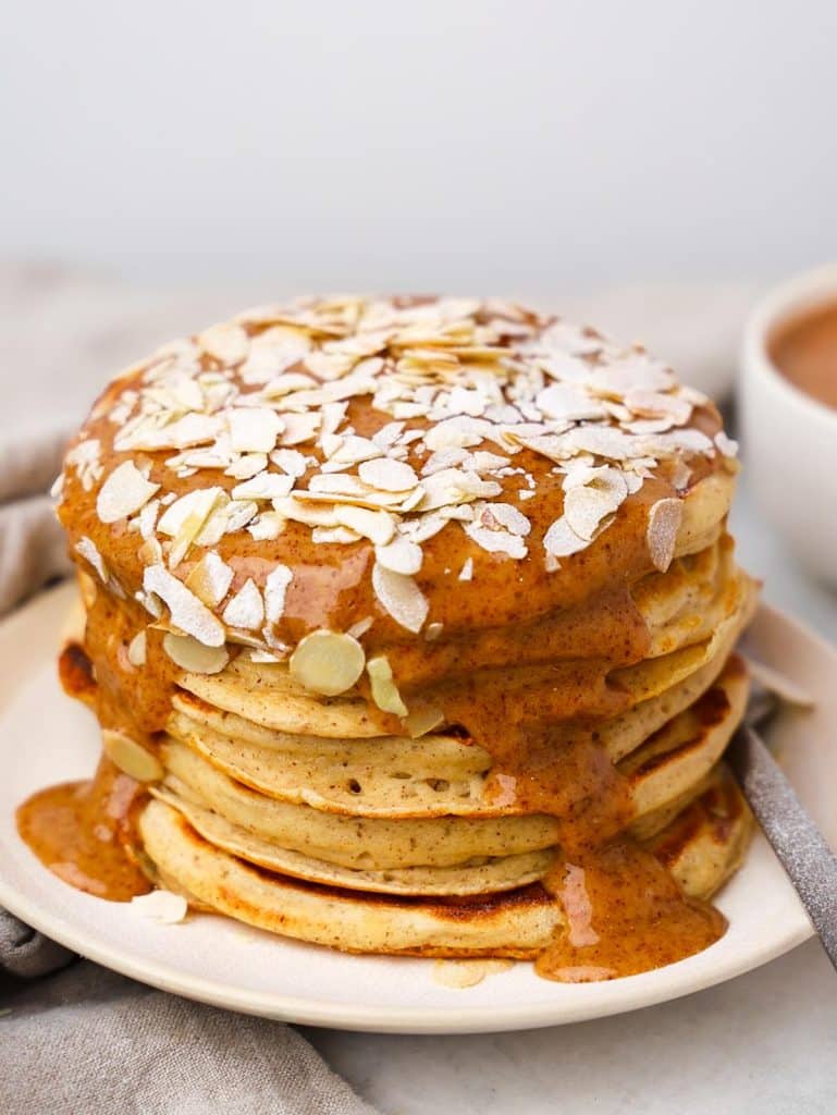 Almond croissant protein pancakes stacked on a white plate with almond butter drizzle and sliced almonds