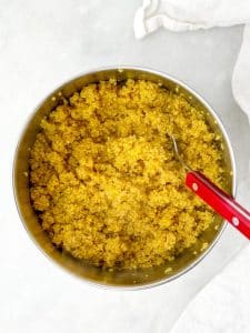 Golden turmeric quinoa in a saucepan with a red spoon