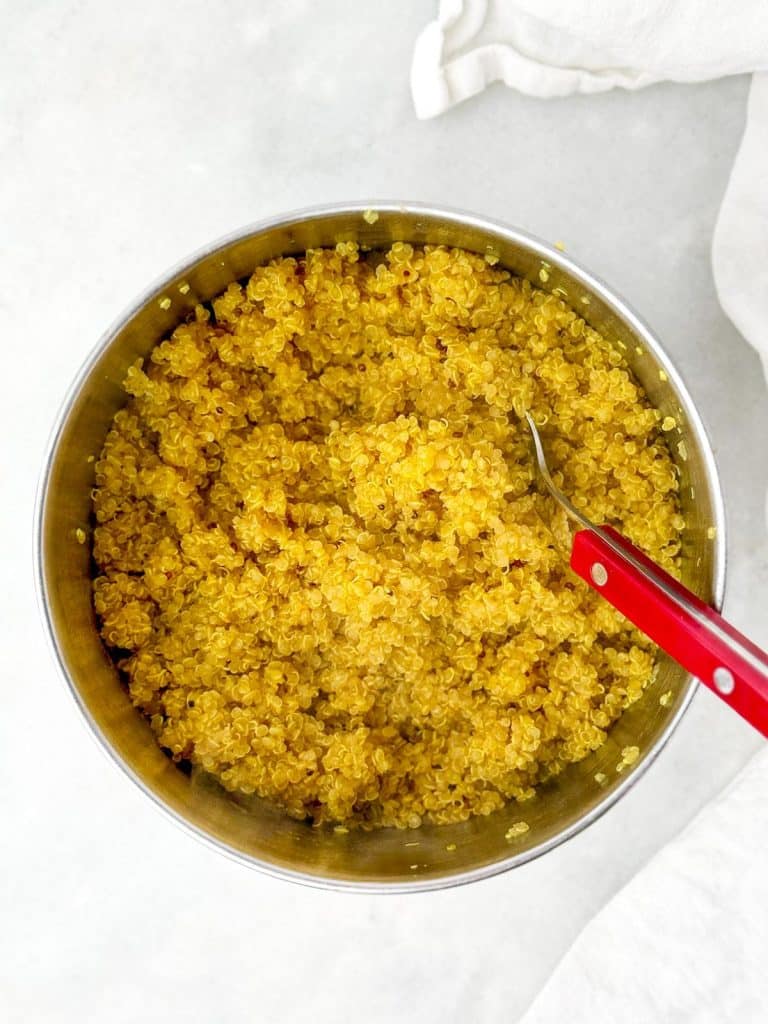 Golden turmeric quinoa in a saucepan with a red spoon