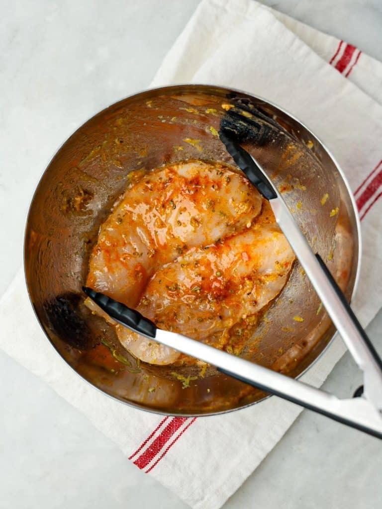 Chicken breast marinating in lemon oregano and olive oil in a mixing bowl