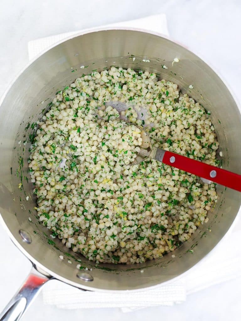 Pot of cooked israeli couscous tossed with fresh dill, parsley, mint, and lemon zest