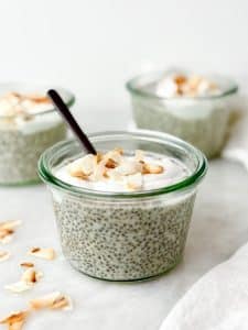 High-protein coconut chia pudding in a glass jar with a spoon topped with coconut yogurt and toasted flakes