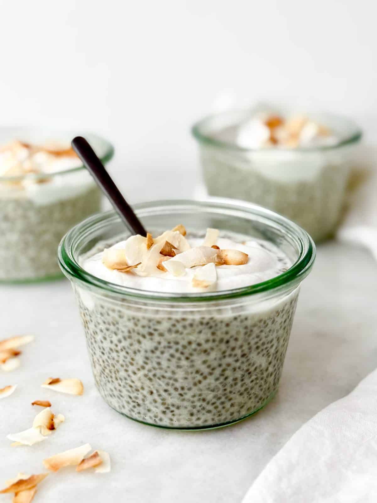 High-protein coconut chia pudding in a glass jar with a spoon topped with coconut yogurt and toasted flakes