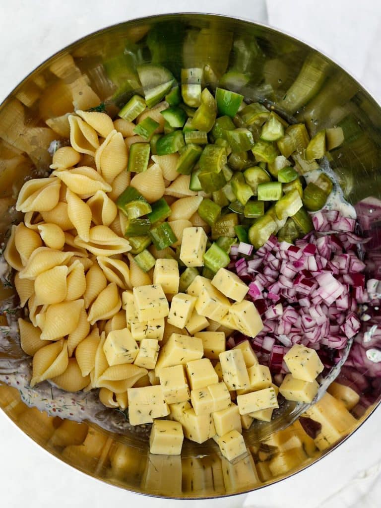 Pasta shells, diced pickles, cubed dill havarti, and red onion in a bowl before tossing