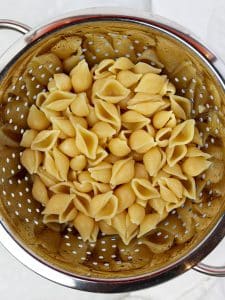 Cooked pasta shells draining in a colander for high-protein dill pickle pasta salad