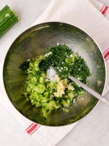 Grated cucumber, fresh dill, garlic, and salt in a bowl for homemade tzatziki