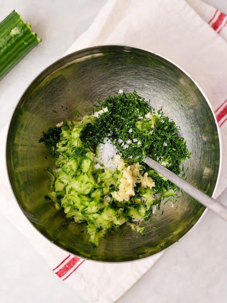 Grated cucumber, fresh dill, garlic, and salt in a bowl for homemade tzatziki