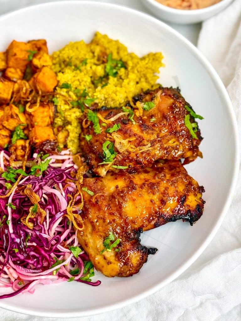 Close-up of caramelized hot honey chicken on a bowl with quinoa and slaw