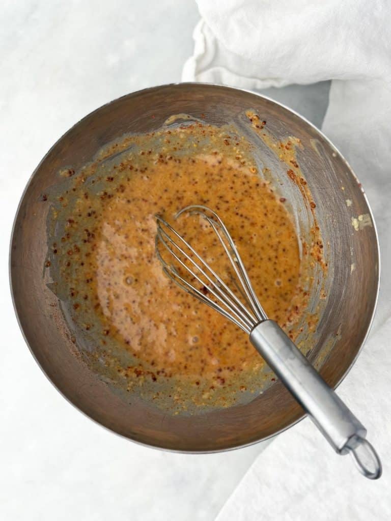 Hot honey mustard sauce with whole grain mustard whisked in a bowl