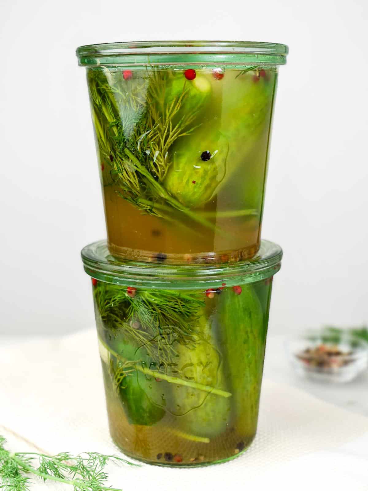 Two stacked Weck jars of lacto fermented garlic dill pickles with fresh dill and peppercorns