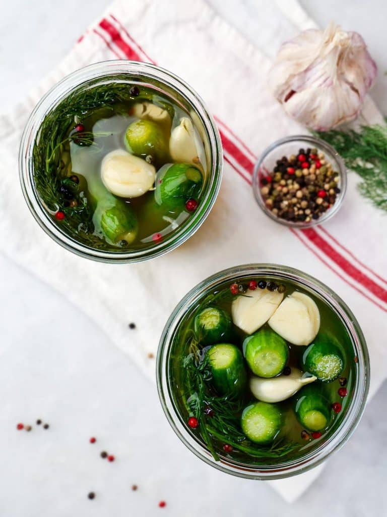 Overhead view of lacto fermented pickles in jars with garlic cloves, dill, and mixed peppercorns