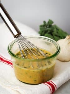 Greek dressing for Mediterranean pasta salad being whisked in a glass jar with fresh herbs and garlic