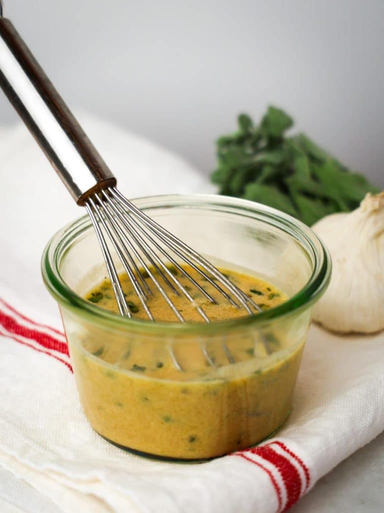 Greek dressing for Mediterranean pasta salad being whisked in a glass jar with fresh herbs and garlic