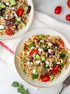 Two white bowls of high protein Mediterranean pasta salad meal prep with cherry tomatoes and fresh herbs