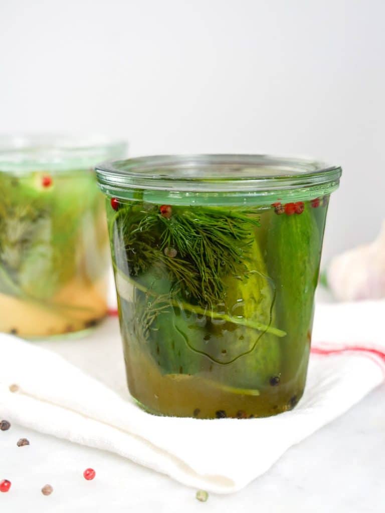 No vinegar fermented dill pickles in a glass jar with garlic and mixed peppercorns