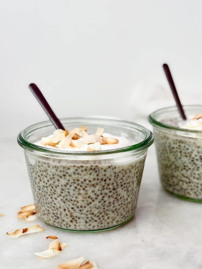 Two jars of protein chia pudding topped with coconut yogurt and toasted flakes