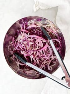 Red and green cabbage slaw tossed with lime juice and tongs