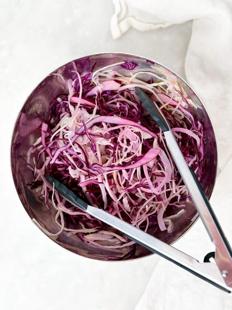Red and green cabbage slaw tossed with lime juice and tongs