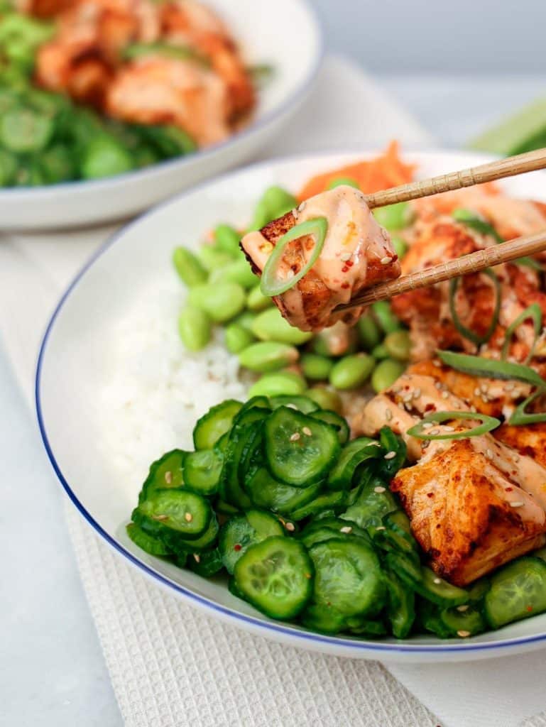 Close up of bang bang salmon bites with cucumber salad and edamame