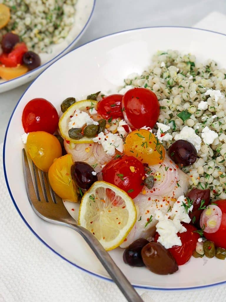 Close-up of Mediterranean cod with herby israeli couscous, feta, olives, capers, and lemon