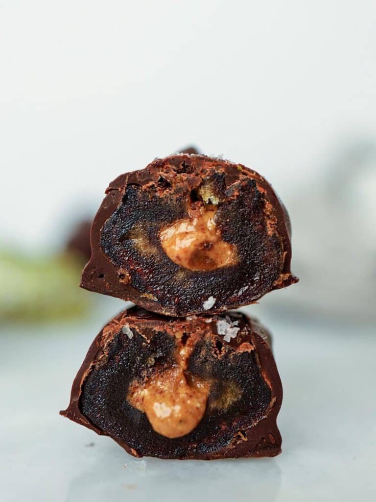Two stacked chocolate covered dates cut in half showing almond butter filling
