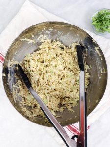 Creamy sesame cabbage slaw tossed with tongs in a stainless steel bowl