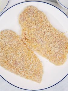 Two panko-breaded chicken cutlets on a plate before air frying