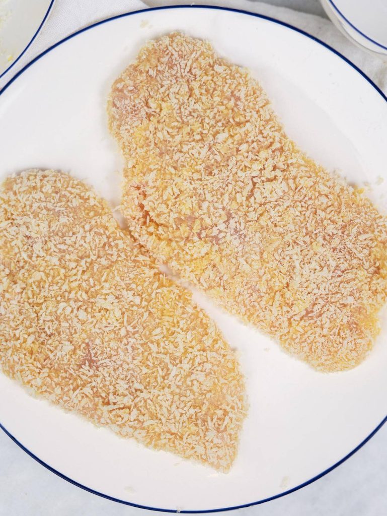 Two panko-breaded chicken cutlets on a plate before air frying