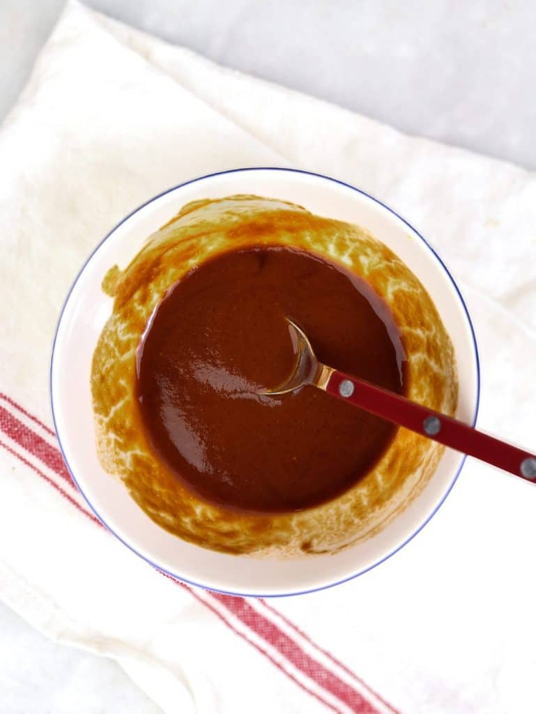 Homemade tonkatsu sauce whisked together in a small white bowl with a red spoon