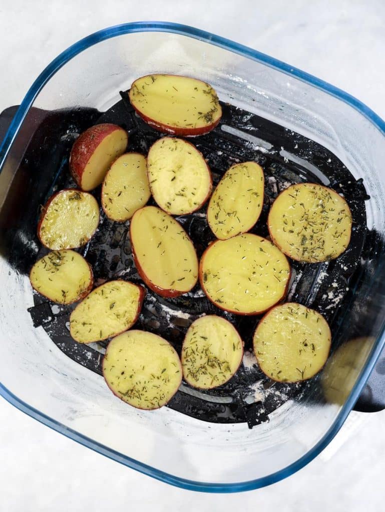 Halved baby potatoes seasoned with garlic powder and rosemary in a clear air fryer basket