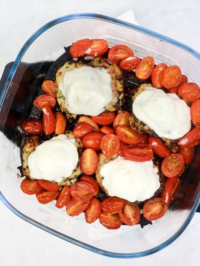 Air fryer pesto chicken with melted mozzarella nestled among burst cherry tomatoes in the basket